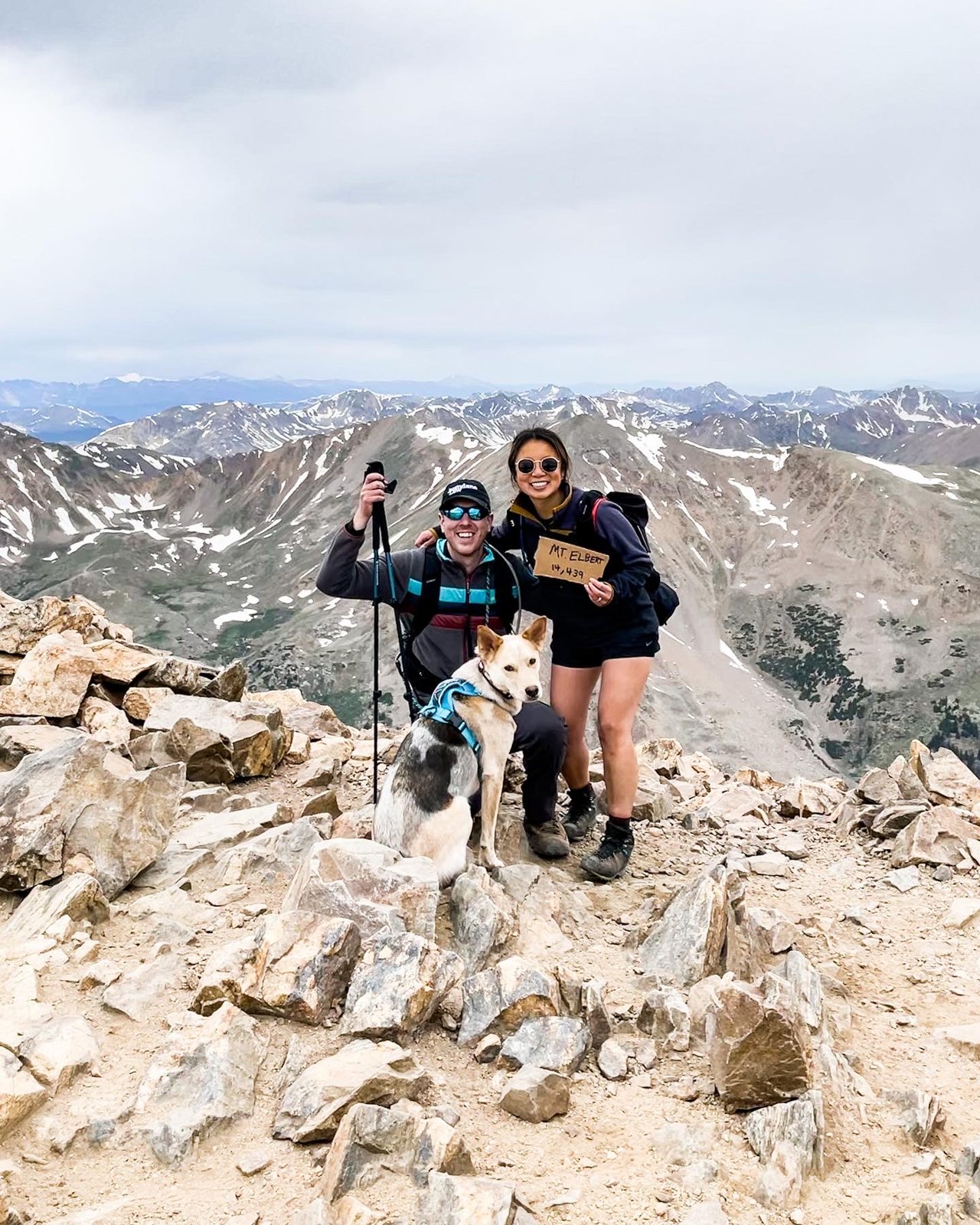 Diana and Toby standing together on a mountain summit with a wide Pacific Northwest panorama behind them